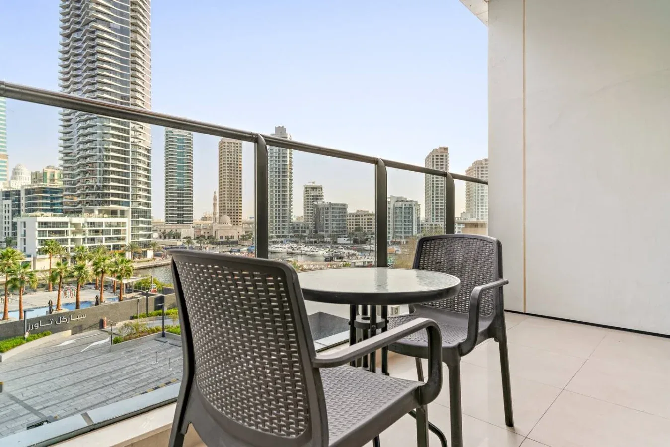 A balcony seating area overlooks a waterfront lined with modern high-rise buildings.