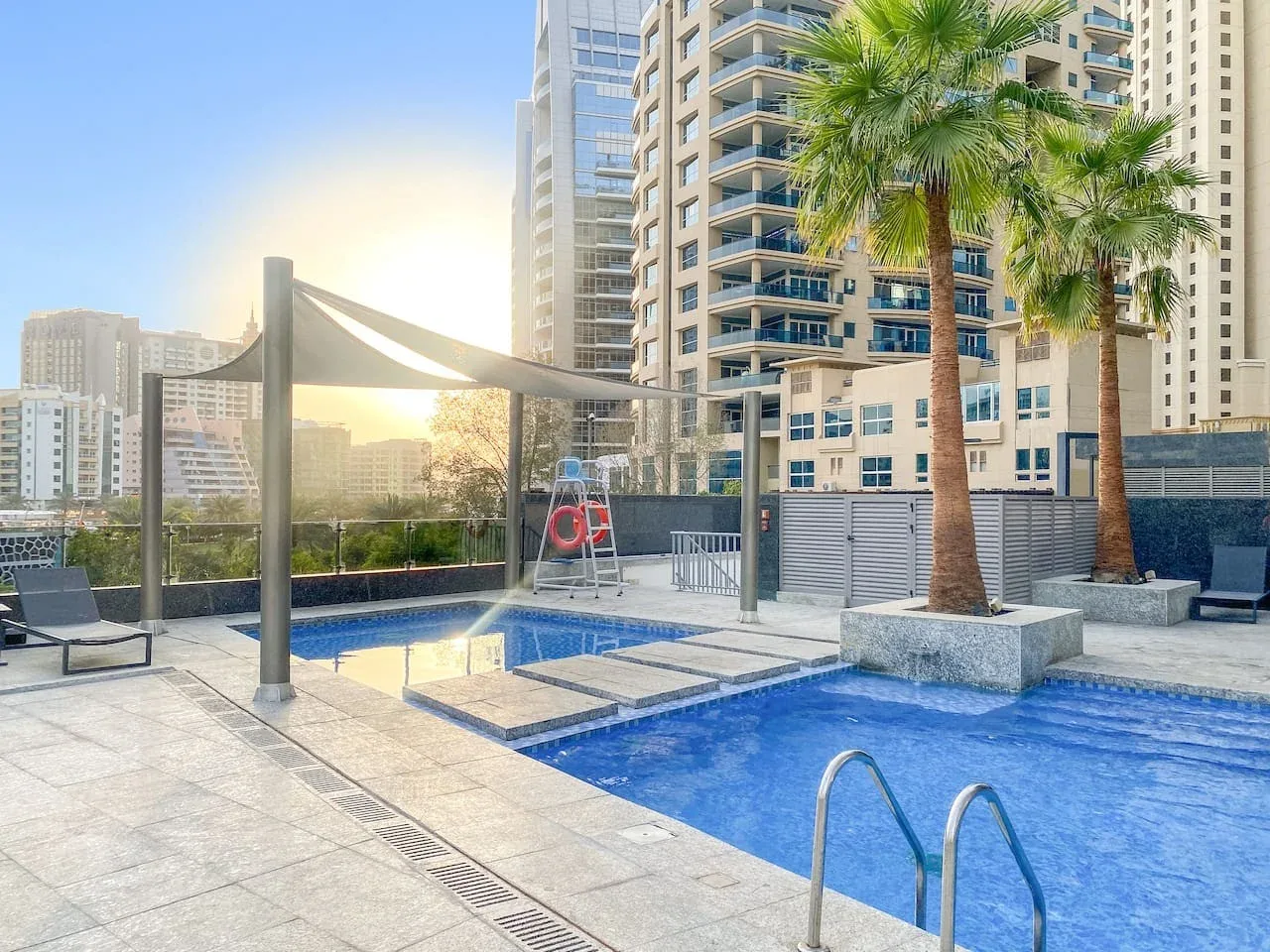 A rooftop pool sits beside high-rise buildings and palm trees.