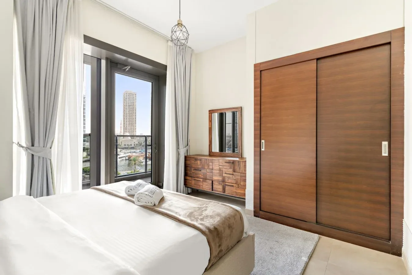 A bedroom with a bed beside a tall window and a wooden wardrobe.
