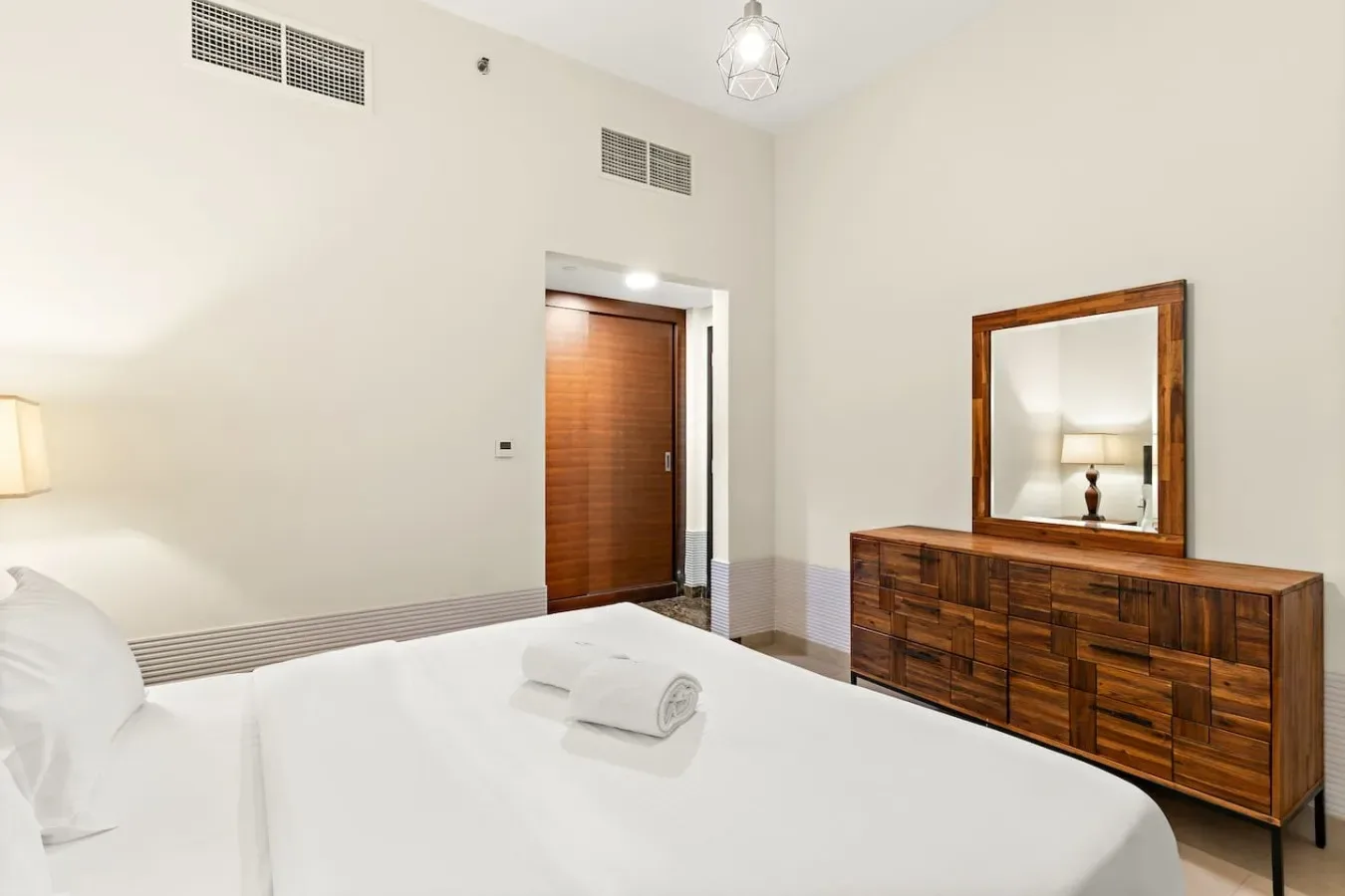 A bright bedroom with a bed and a wooden dresser beneath a mirror.