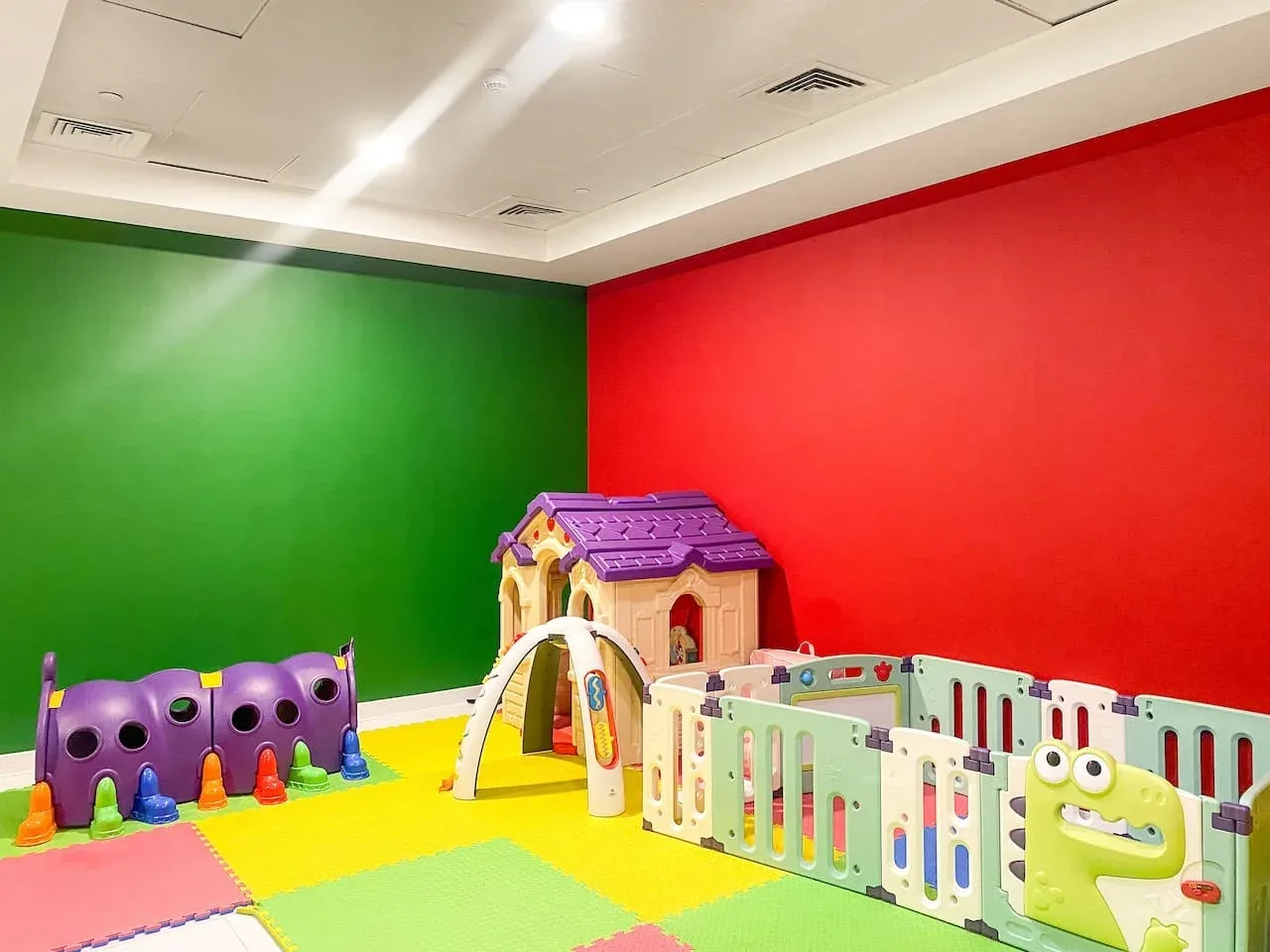 A colorful indoor play area has foam flooring and a fenced children's play zone.