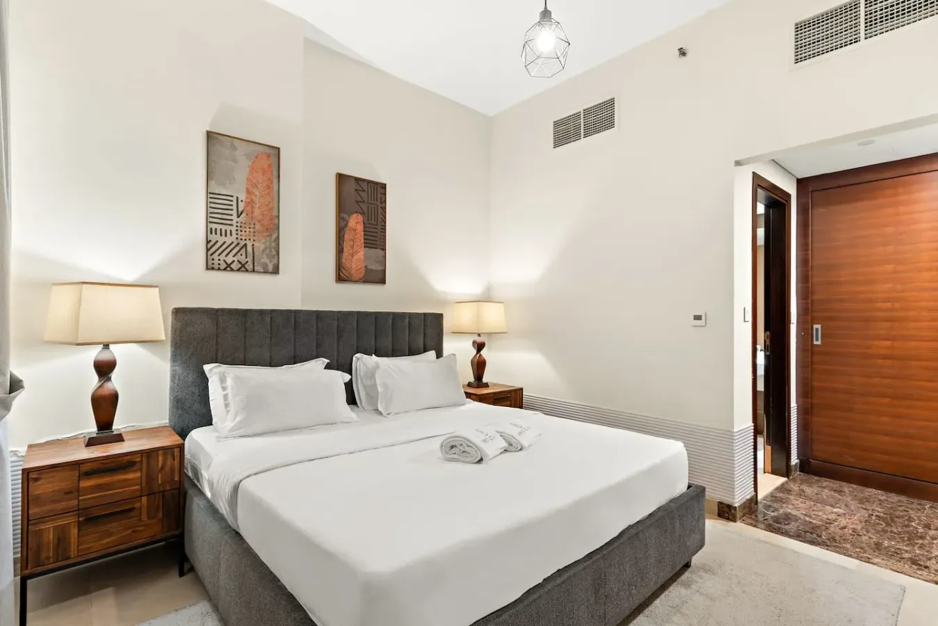 A bright bedroom with a neatly made bed, bedside tables, and wall art.