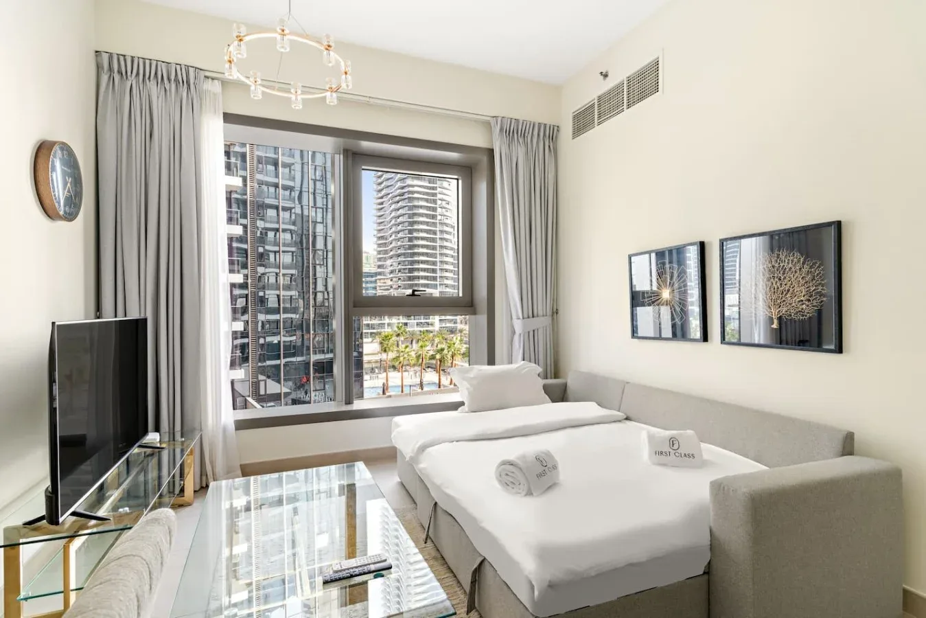 A bedroom with a bed, seating, and large windows overlooking nearby buildings.