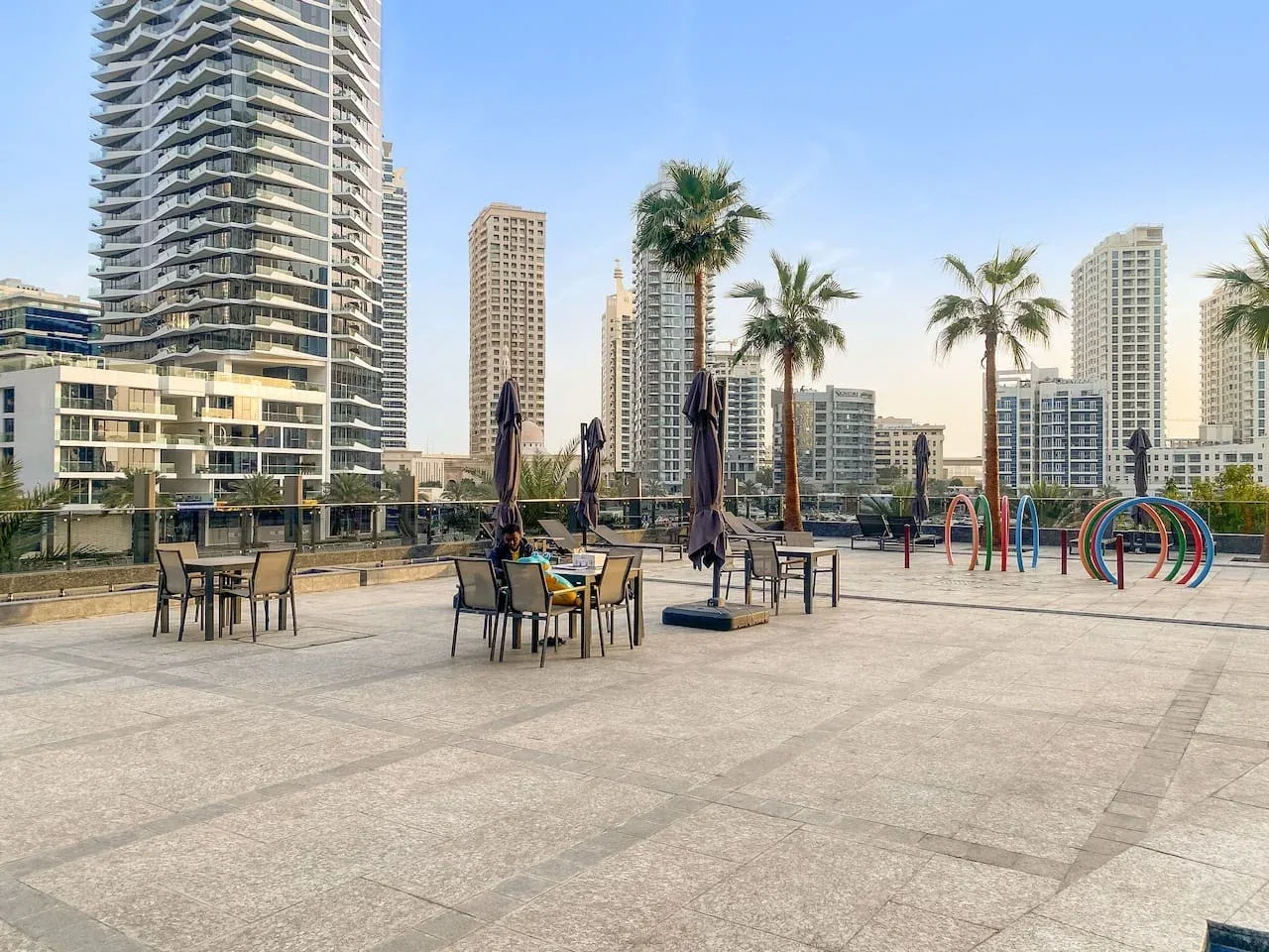 An outdoor terrace with tables and seating overlooks nearby high-rise buildings.