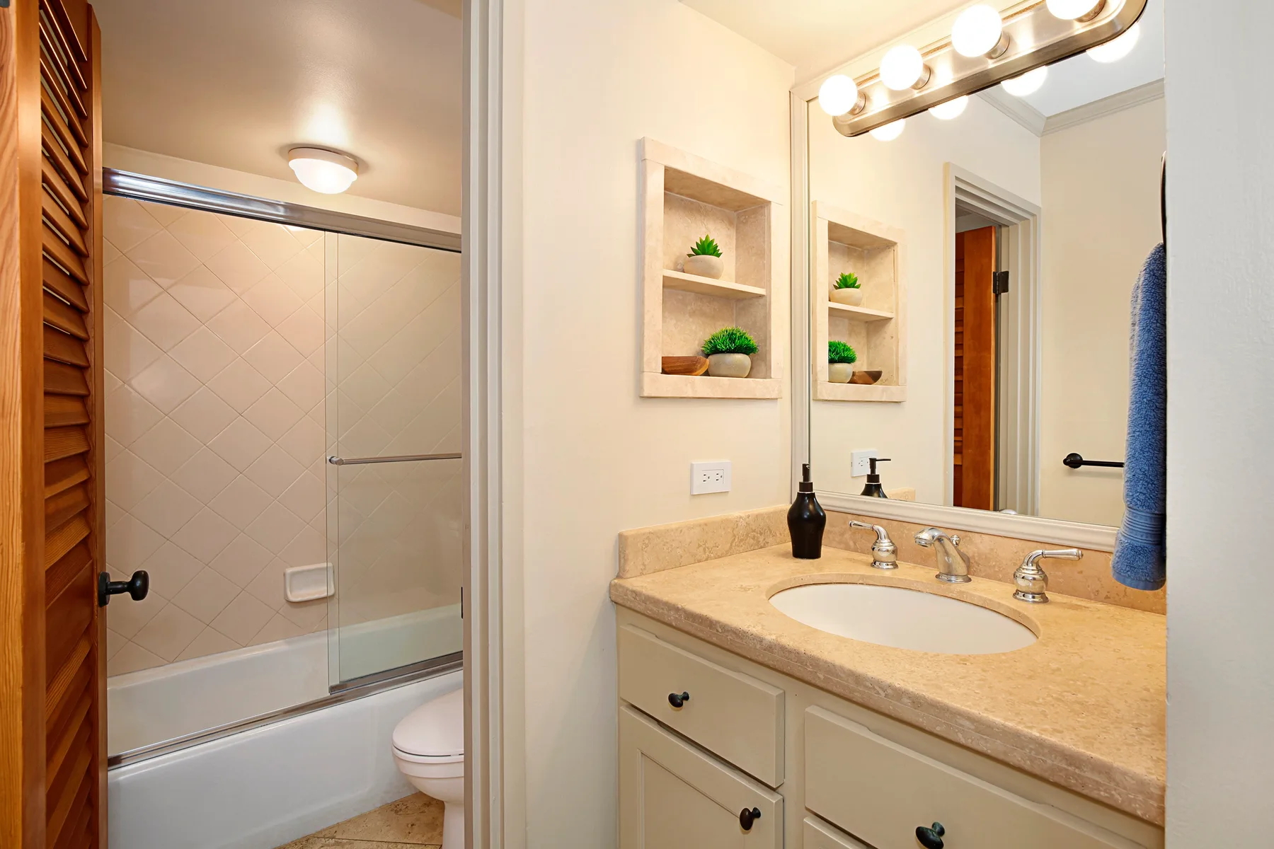 Un lavabo de baño con un fregadero y una bañera visible a través de la puerta.
