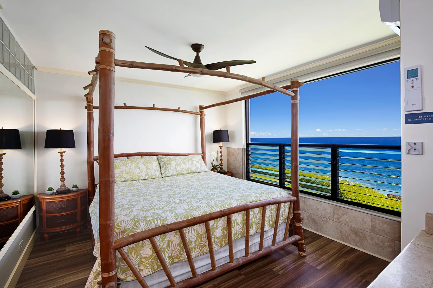 Un dormitorio con una cama con dosel de madera frente a una gran ventana con vista al mar.