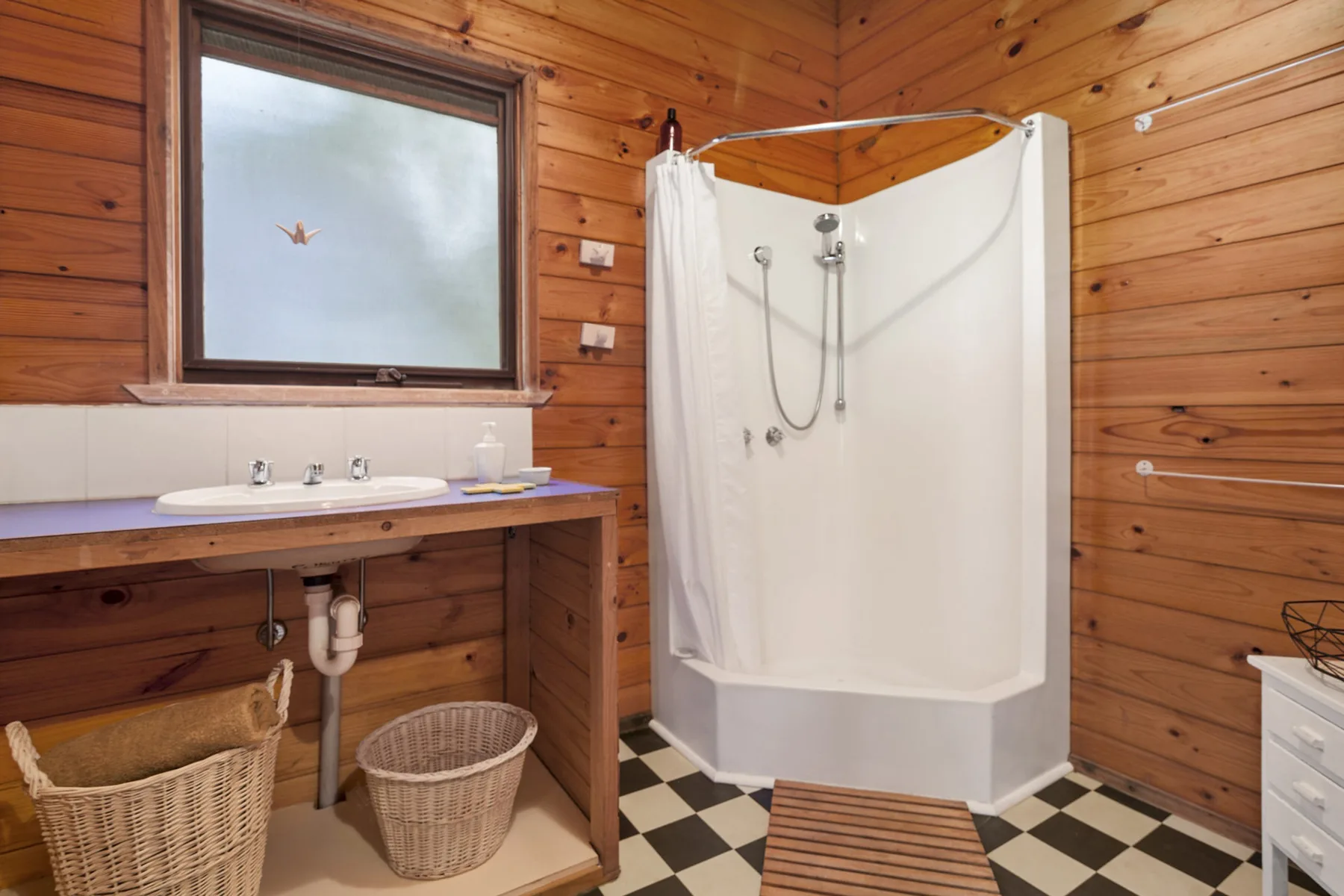 Un baño con lavabo y ducha junto a paredes revestidas de madera.