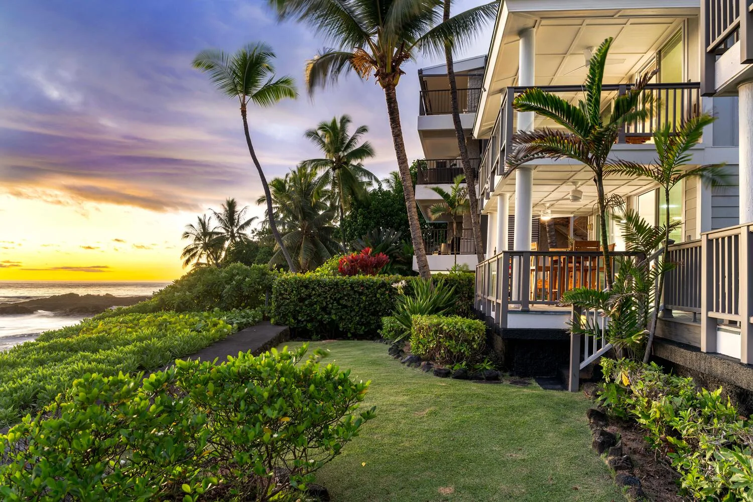 Un jardín tropical ajardinado bordea un edificio junto al océano al atardecer.