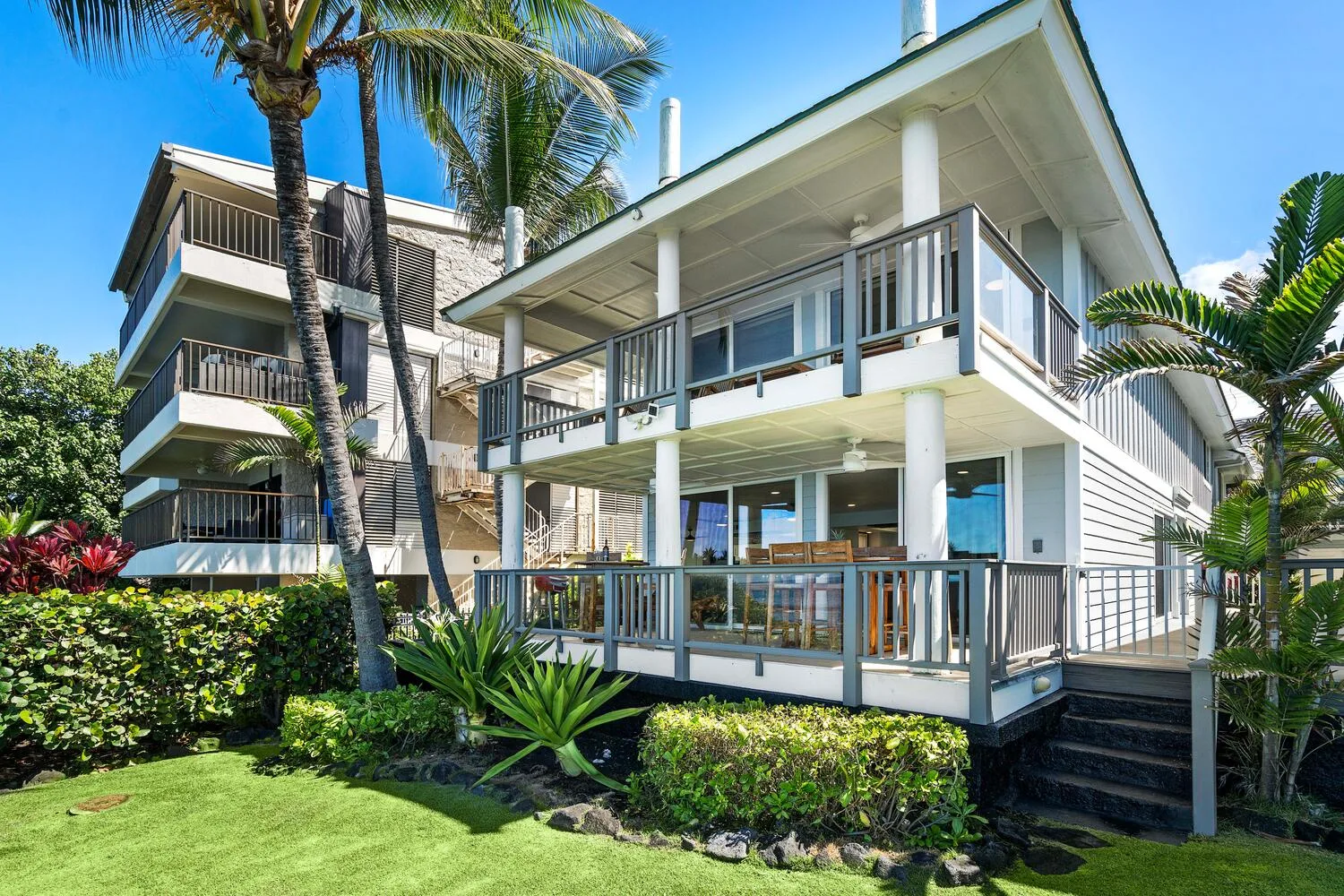 Una casa moderna de dos plantas con balcones envolventes rodeada de vegetación tropical.