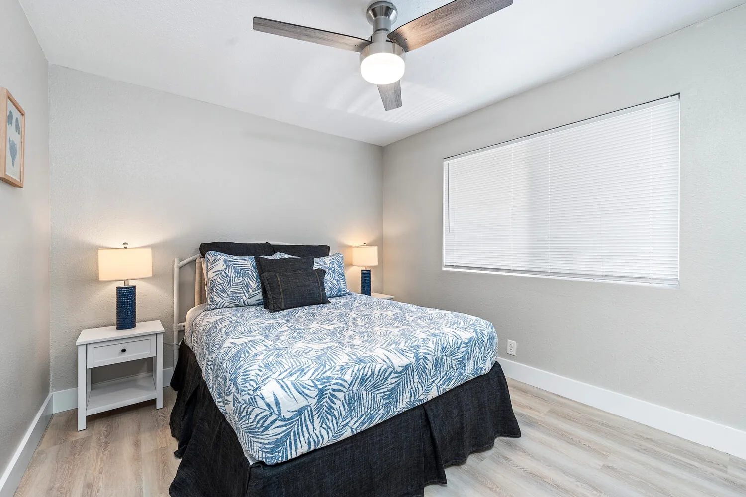 Un dormitorio con una cama vestida con ropa de cama estampada azul y blanca y una ventana con persianas.
