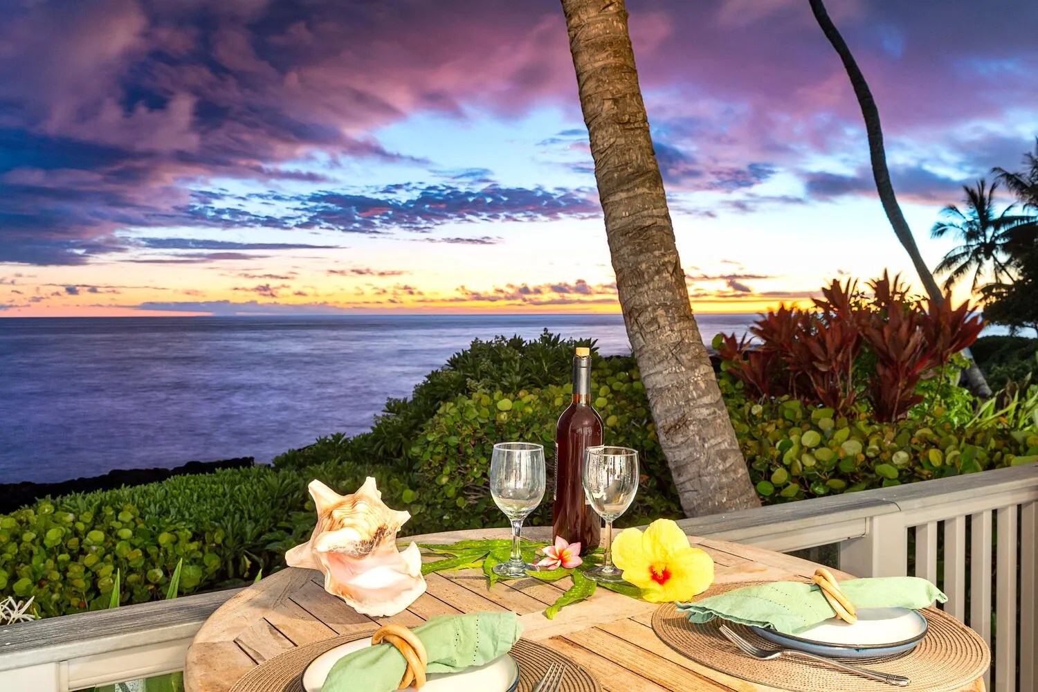 Una mesa de comedor junto al mar, con vino y flores, mira al océano al atardecer.