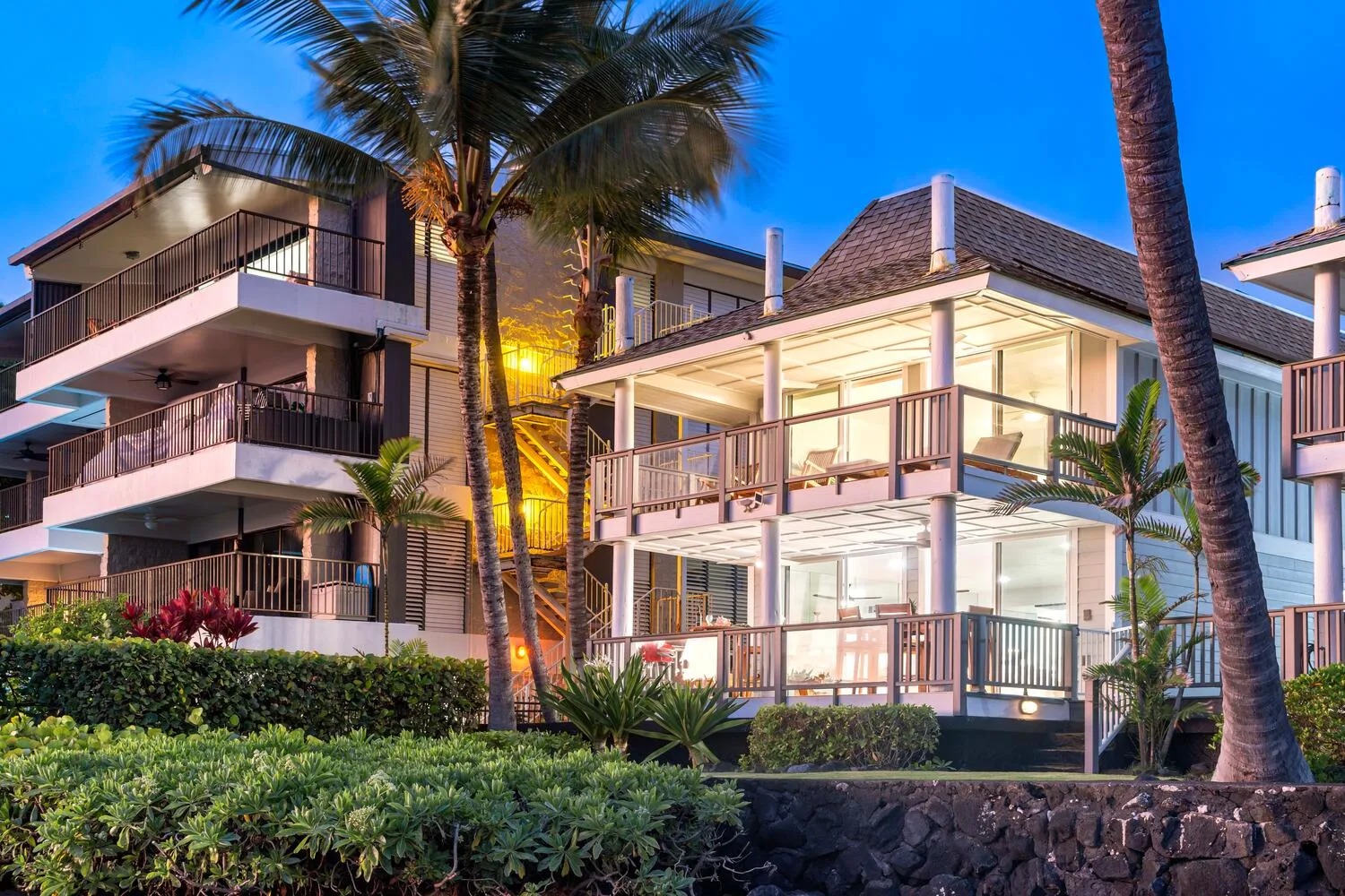 Edificios residenciales modernos con balcones se alzan entre palmeras al anochecer.