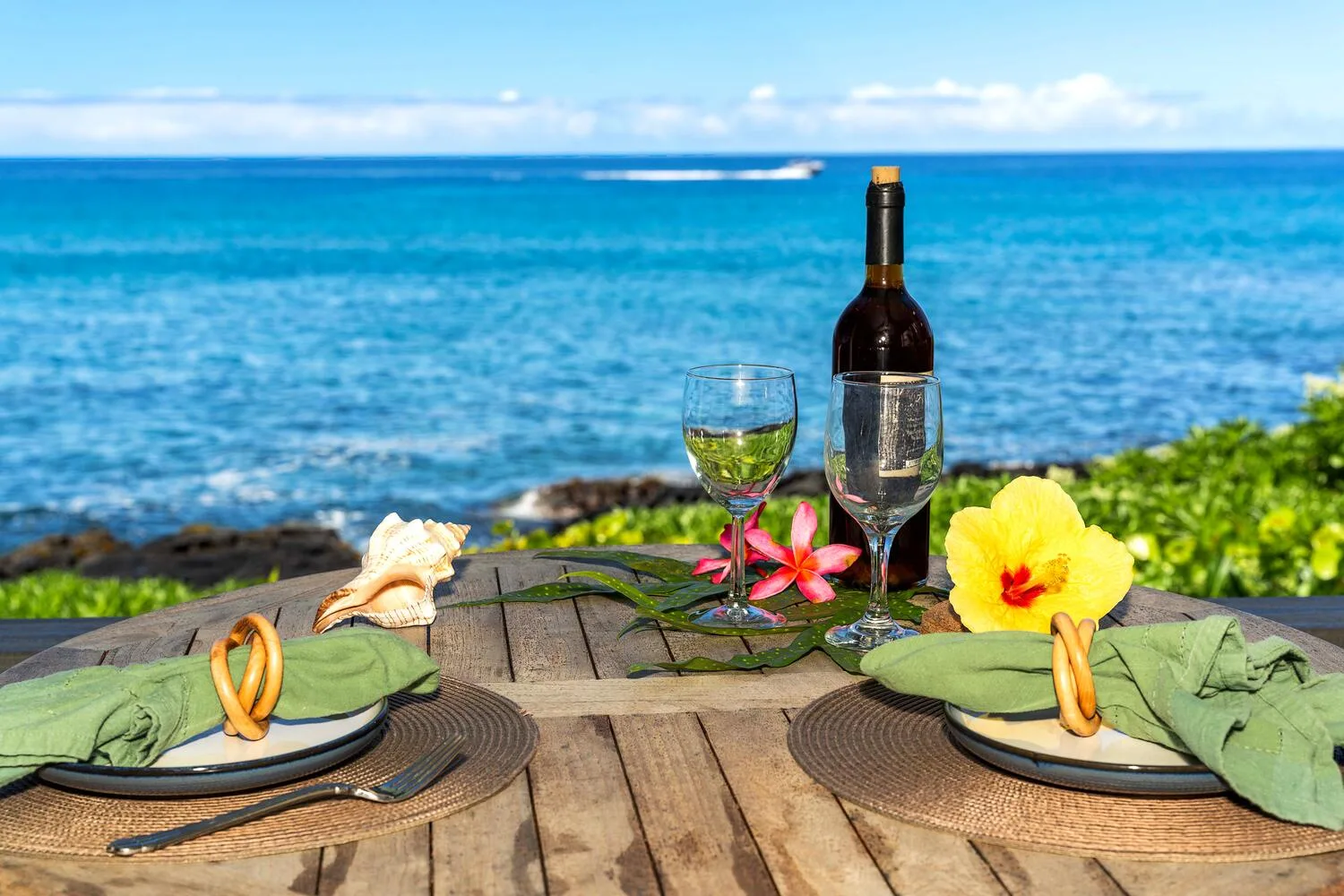 Una mesa junto al mar está puesta con platos, copas de vino y flores frente al océano.