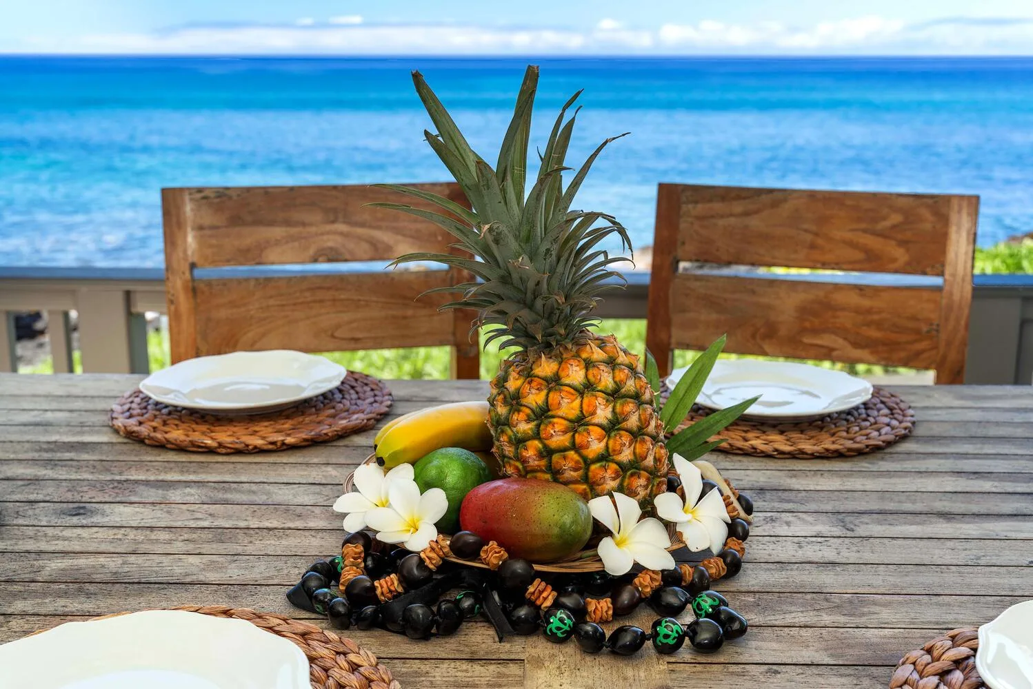 Un arreglo de frutas tropicales está sobre una mesa al aire libre con vista al mar.