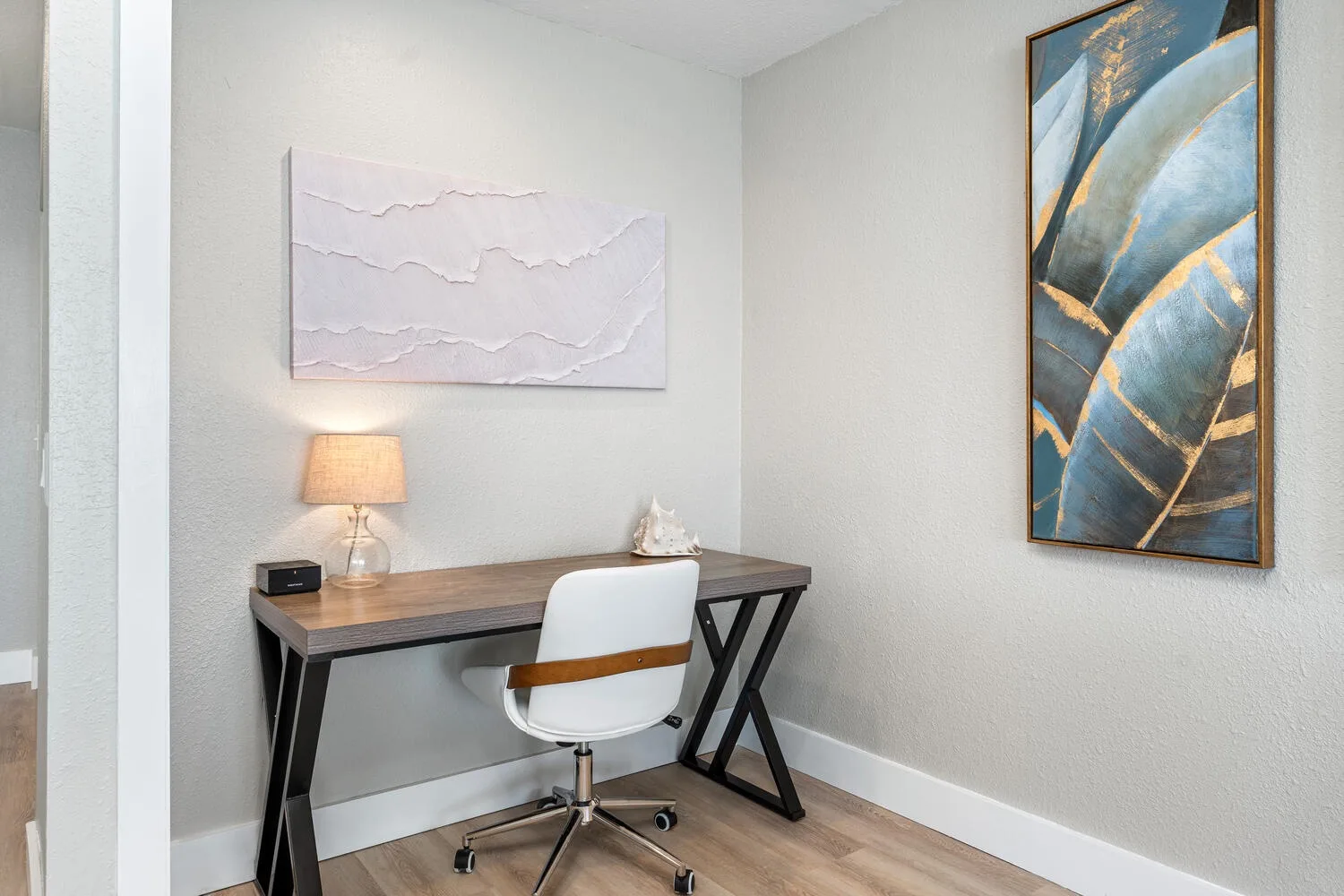 Un pequeño espacio de trabajo tiene un escritorio, una silla blanca y arte abstracto en la pared.