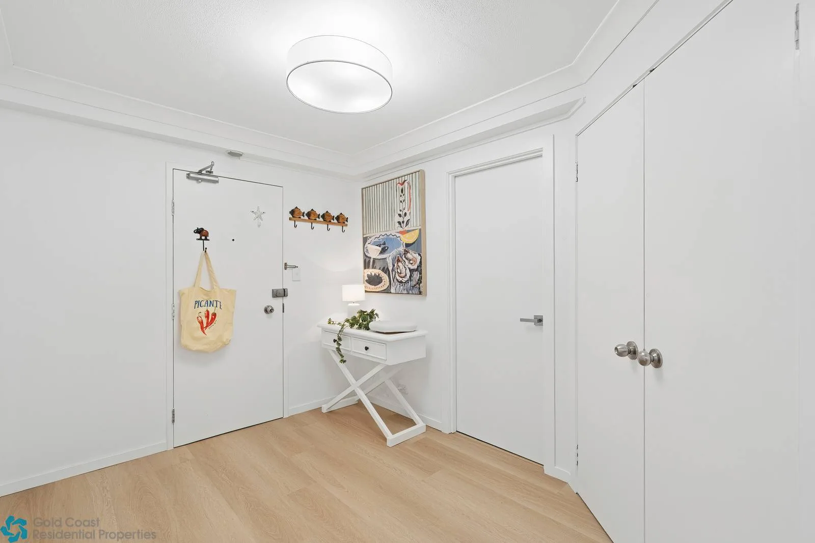 Una entrada blanca y luminosa con un lavabo pequeño y ganchos en la pared.