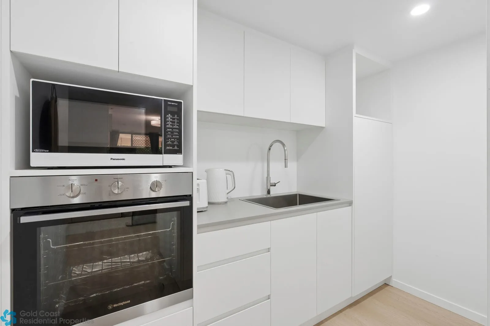 Una cocina blanca y luminosa con horno, microondas y fregadero.