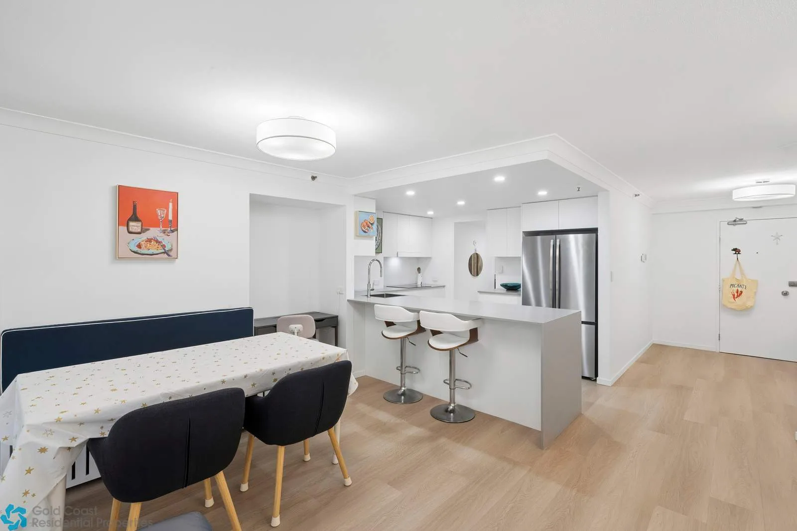 Comedor de planta abierta y cocina con mesa, barra y refrigerador de acero inoxidable.