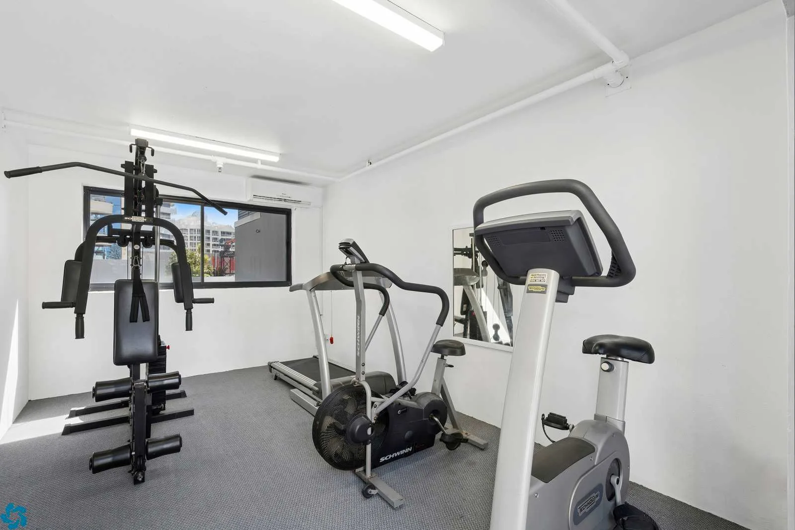 Un gimnasio interior luminoso con máquinas de ejercicio y una ventana.