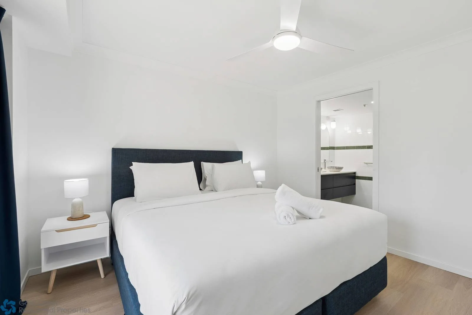 Un dormitorio luminoso con una cama bien tendida y una puerta abierta hacia un baño.