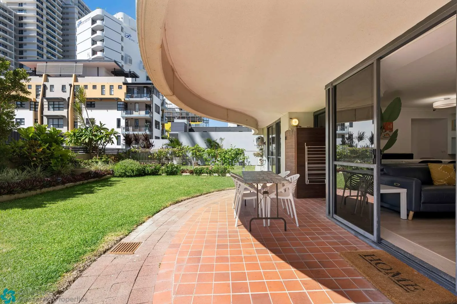 Un patio de baldosas con asientos al aire libre da a un césped verde y edificios cercanos.