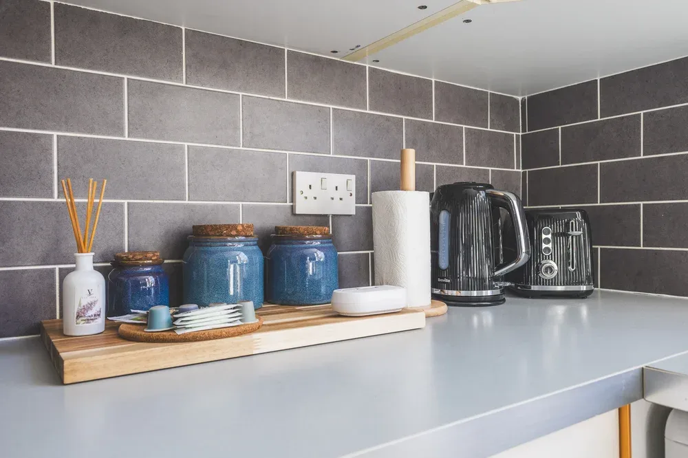A kitchen counter holds a kettle, toaster, and a tray of small items.