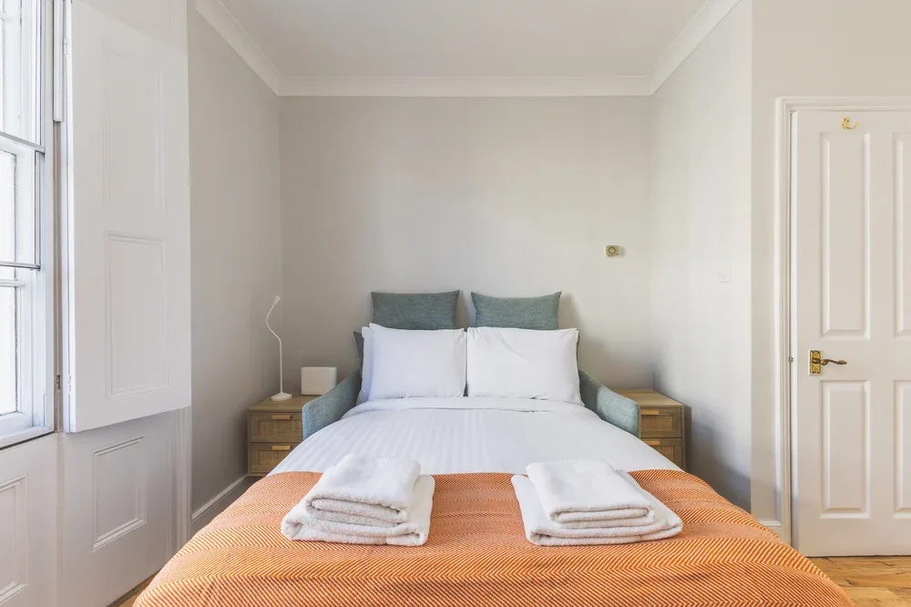 A bedroom with a neatly made bed and folded towels at the foot.