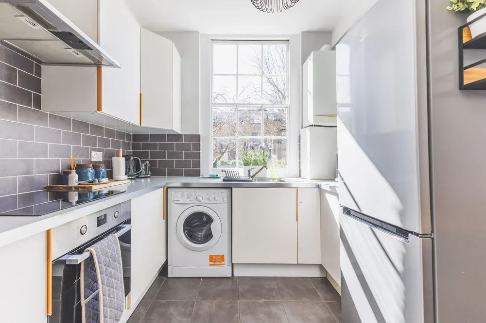 A bright kitchen with white cabinets, dark tile backsplash, and a washing machine.