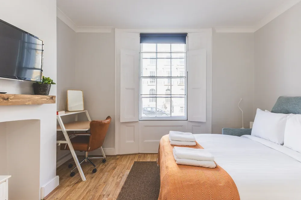 A bright bedroom with a bed, window, and compact desk area.
