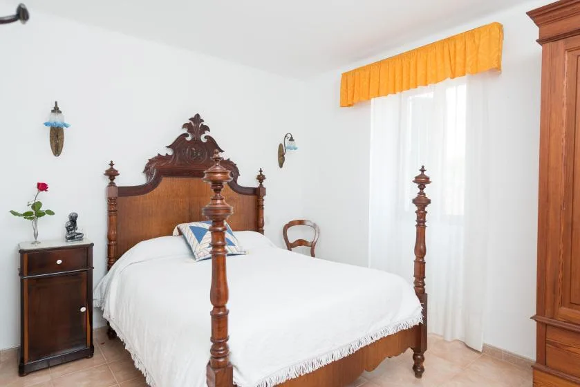 A bedroom with a wooden bed, white bedding, and a bright curtained window.