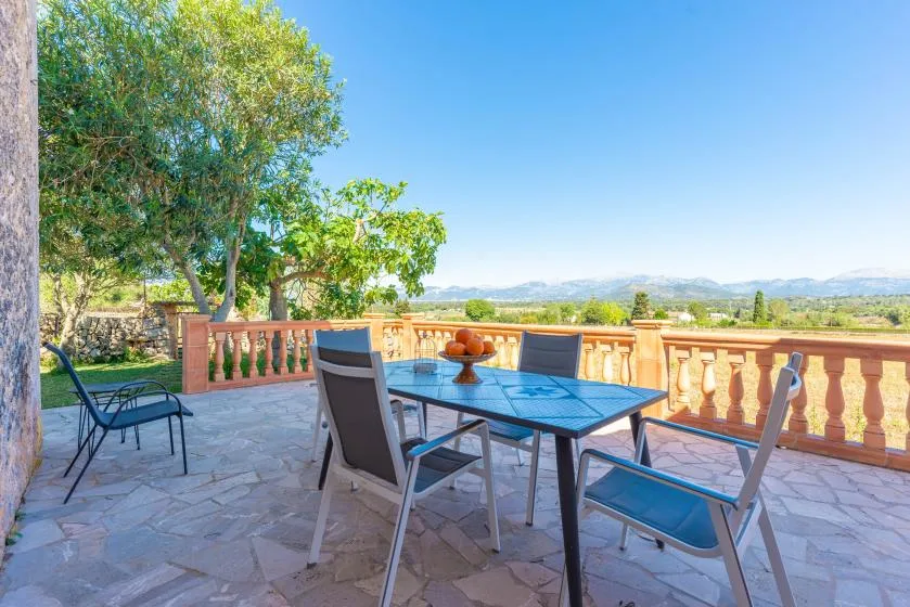 A tiled outdoor terrace has a dining table and seating overlooking a green landscape.