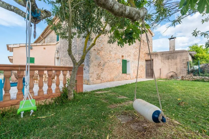 A grassy courtyard beside a stone building, with a swing hanging from a tree.