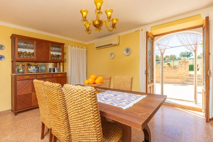 A dining room with a wooden table and woven seating beside open patio doors.