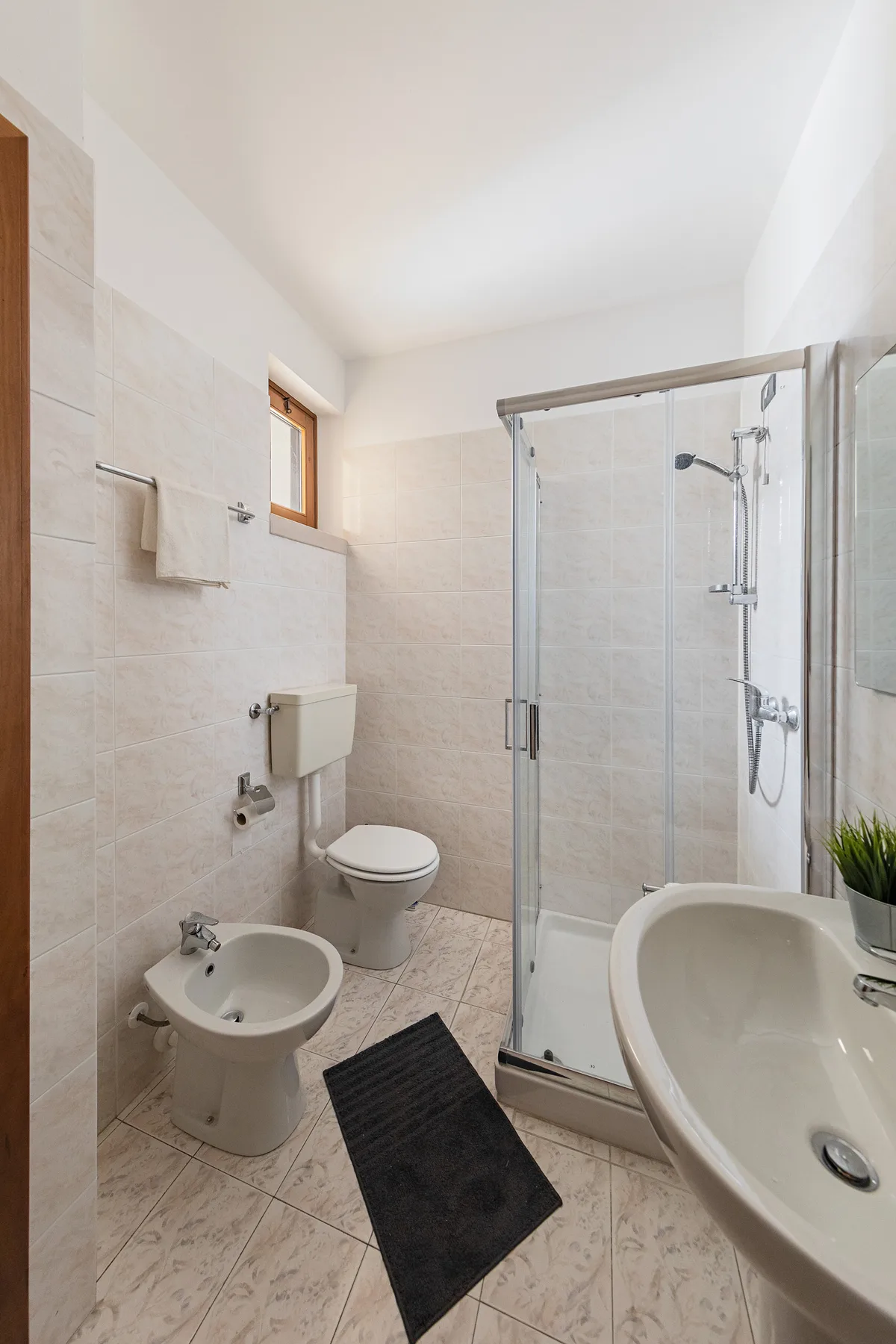 A tiled bathroom with a glass shower, toilet, bidet, and sink.