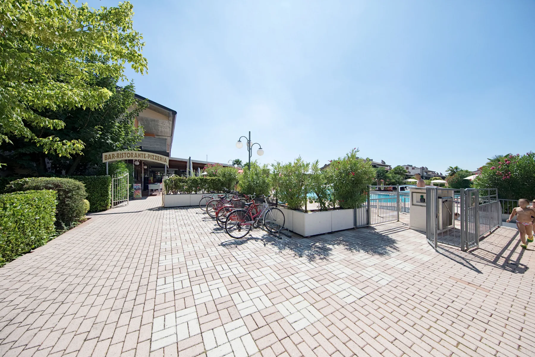 A paved outdoor pool area with planters, bicycles, and a gated entrance.