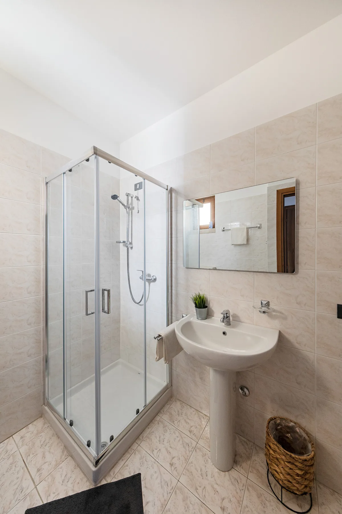 A tiled bathroom with a glass shower and a pedestal sink.