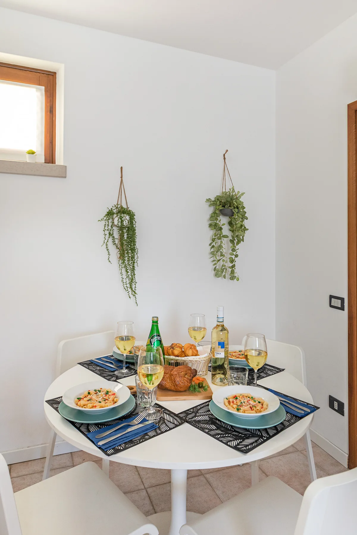 A dining area with a round table set with plates, glasses, and food.