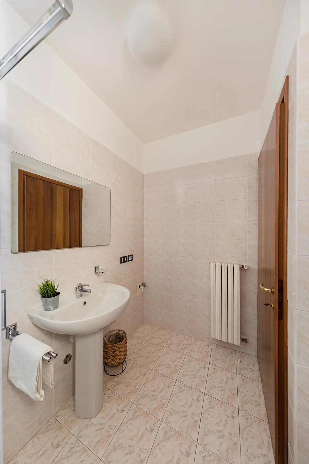 A tiled bathroom with a pedestal sink, mirror, and wall-mounted radiator.