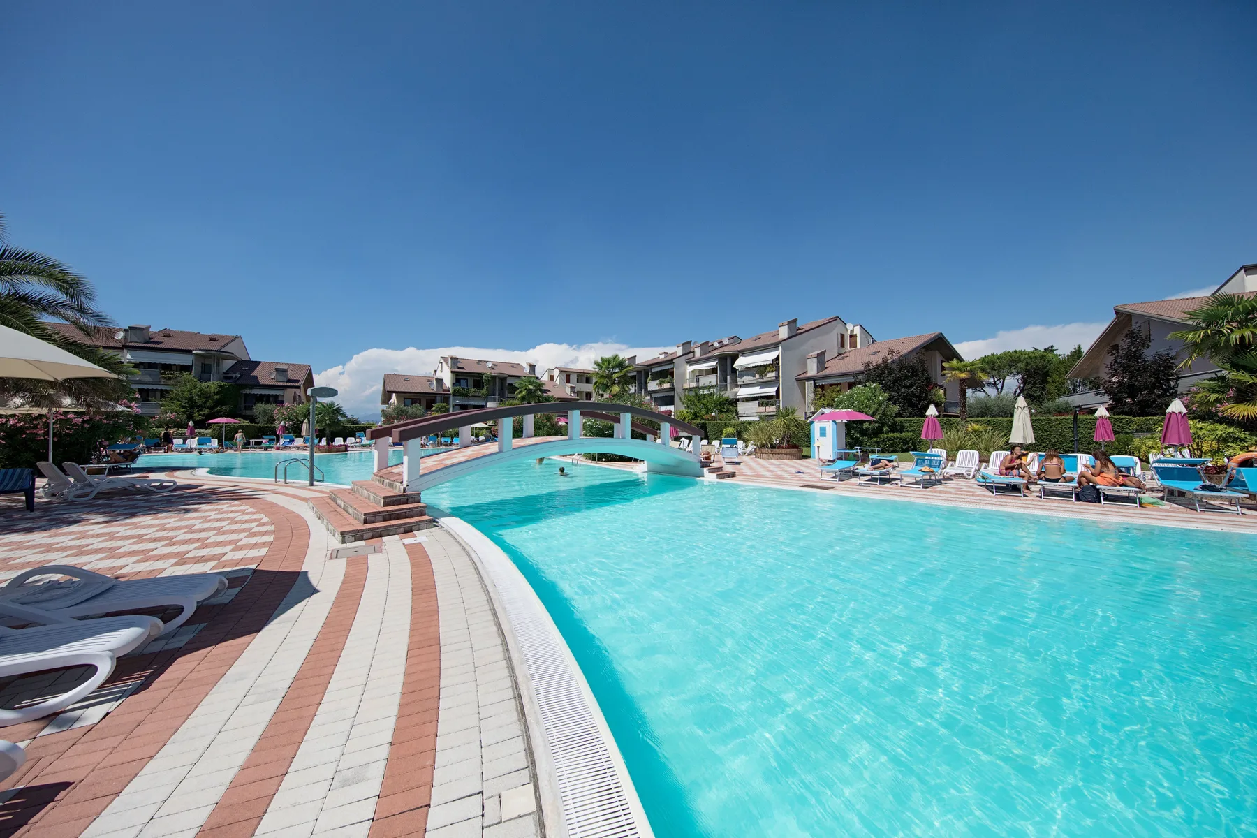 An outdoor swimming pool with a small arched bridge and lounge chairs nearby.