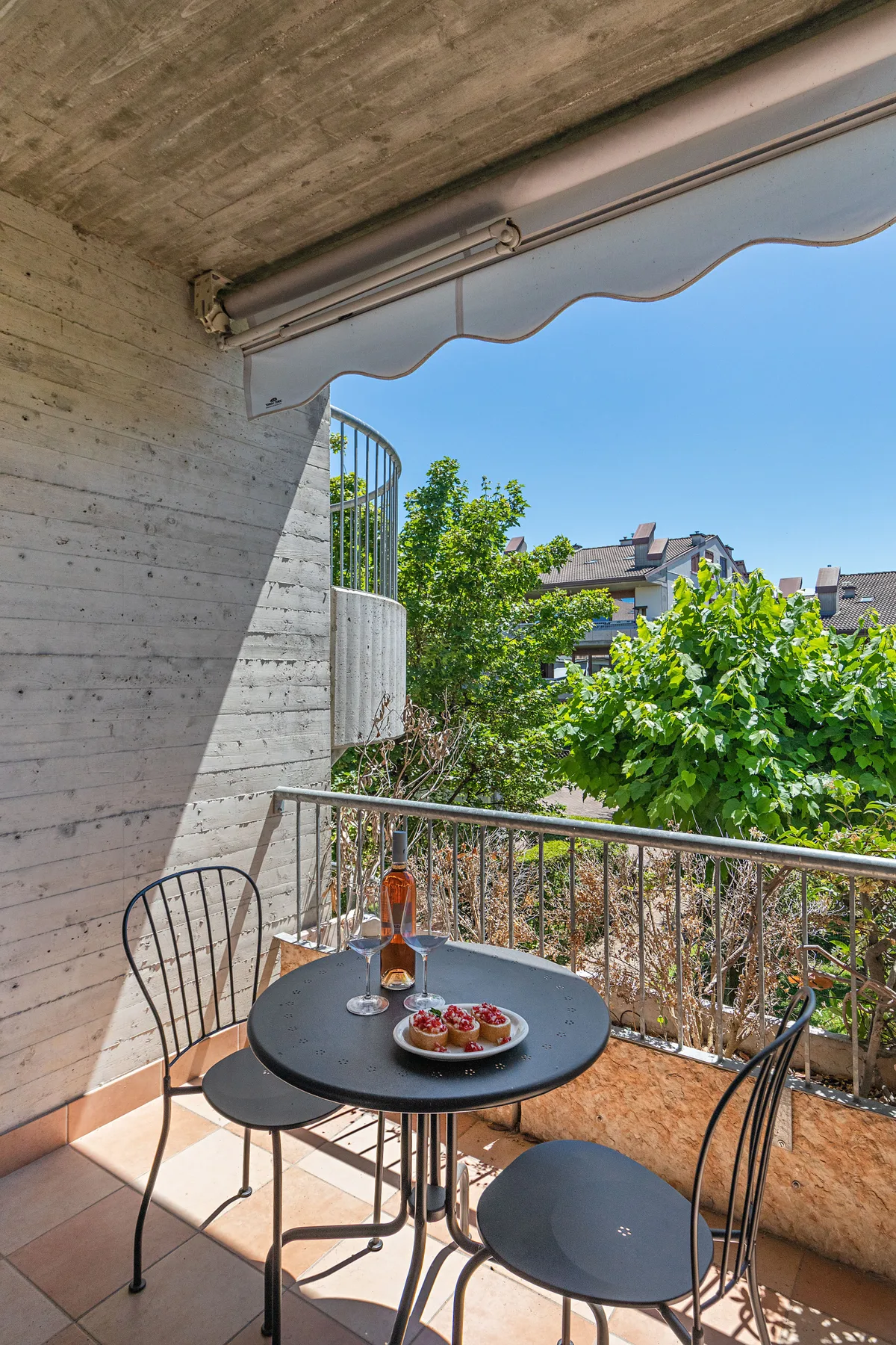 A balcony seating area has a small table and a leafy view.
