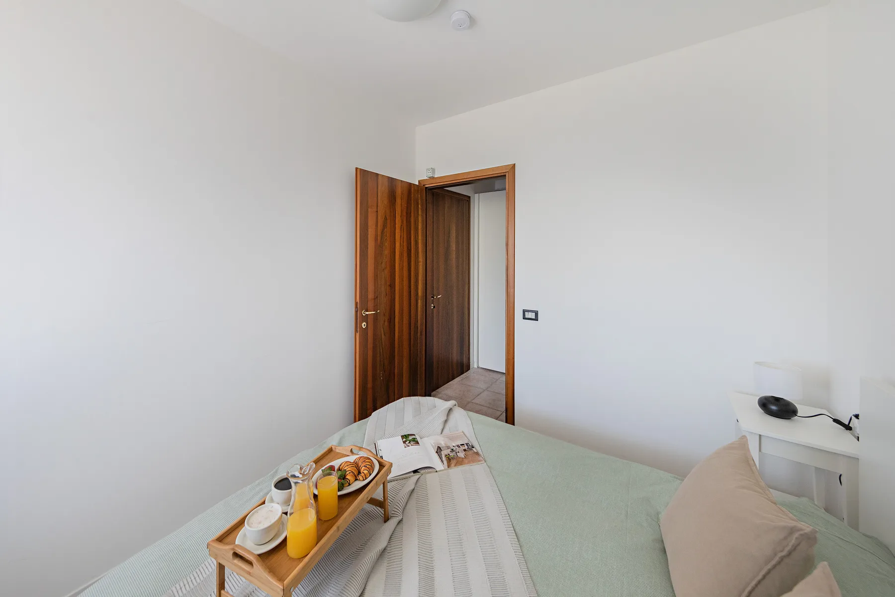 A bright bedroom with a made bed and an open wooden door.