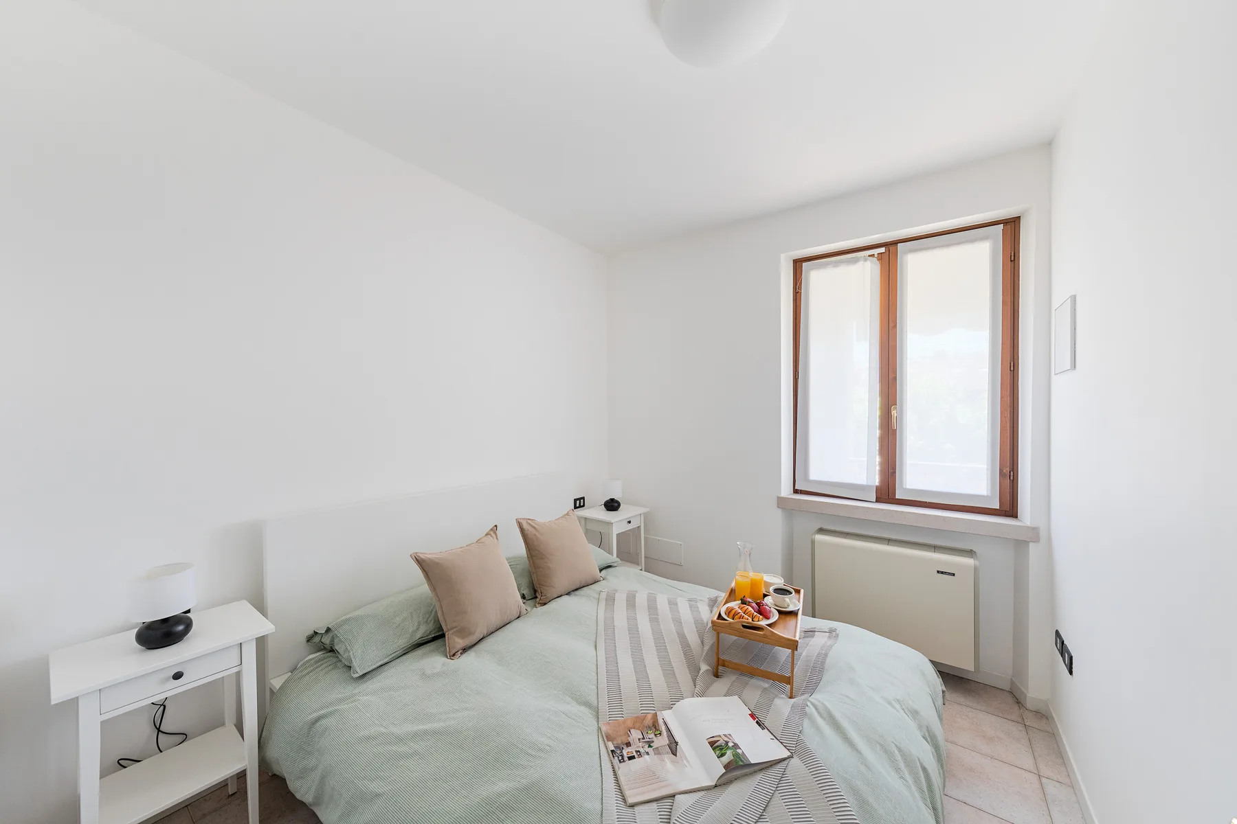 A bright bedroom with a bed, bedside tables, and a window.