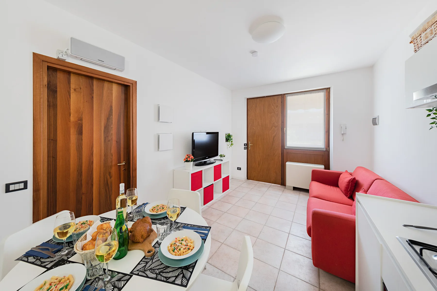 A bright dining and living area with a table, red seating, and a television.