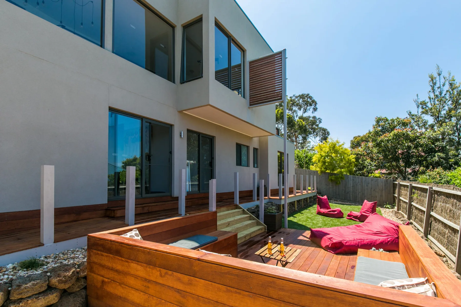 Una casa moderna da a una terraza de madera con asientos exteriores de color rosa intenso.