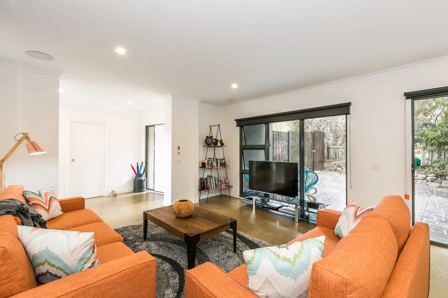 Una sala luminosa con asientos naranjas y un televisor junto a las ventanas.