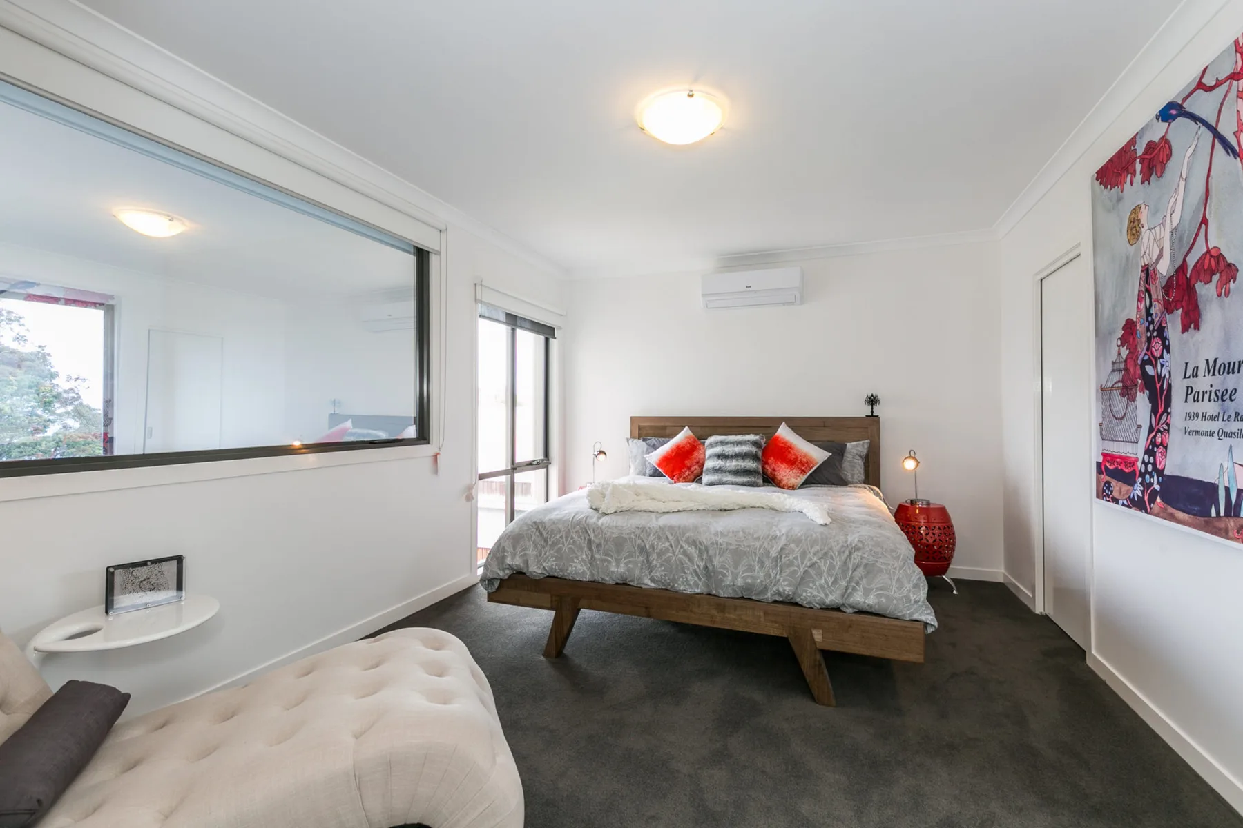 Un dormitorio con una cama, una ventana interior grande y un asiento tapizado de color claro.