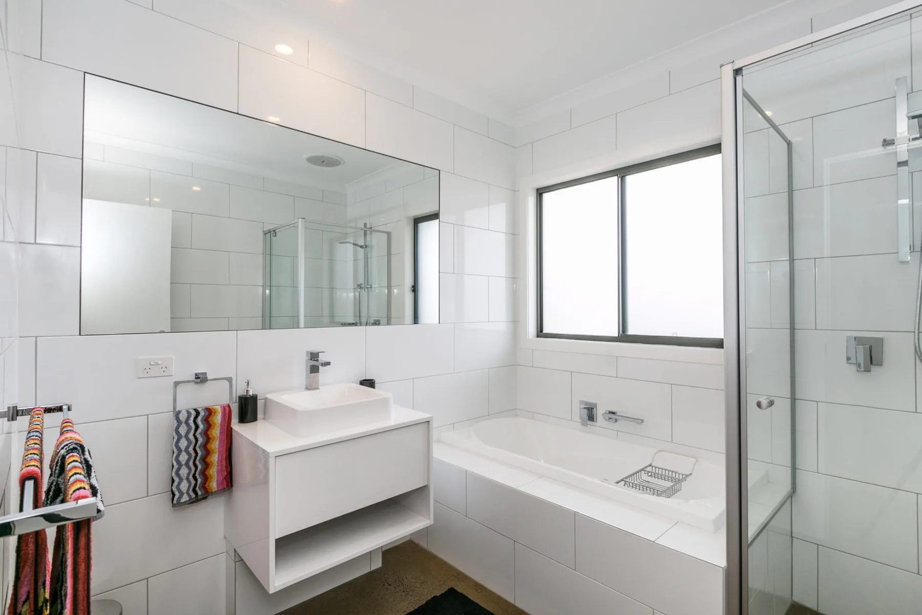 Un baño luminoso con azulejos, bañera, ducha de vidrio y lavabo.