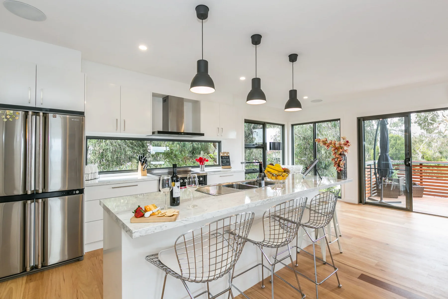 A bright kitchen with a central island, pendant lights, and glass doors opening onto a deck.