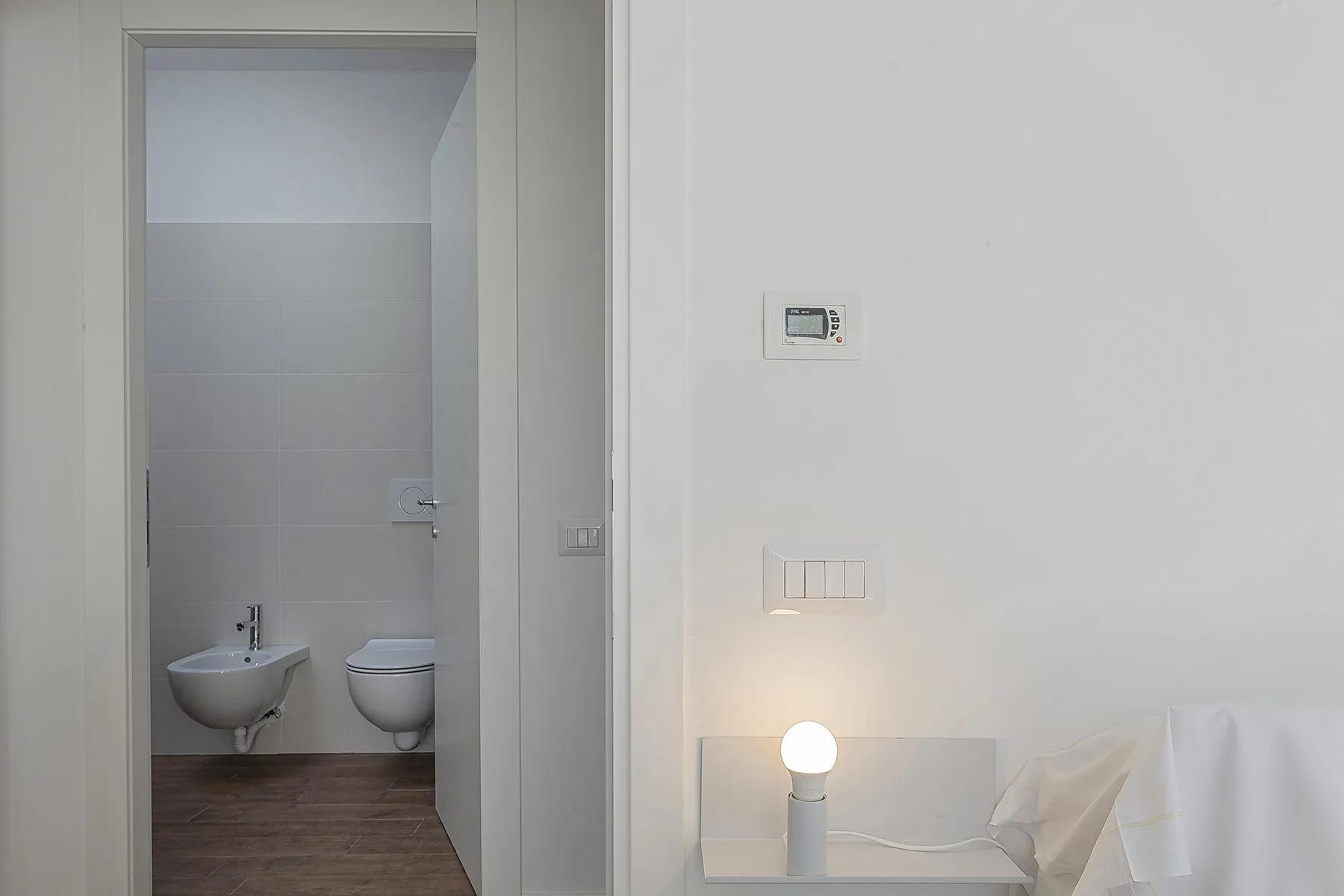 Se ve un baño a través de una puerta abierta, junto a una lámpara encendida.