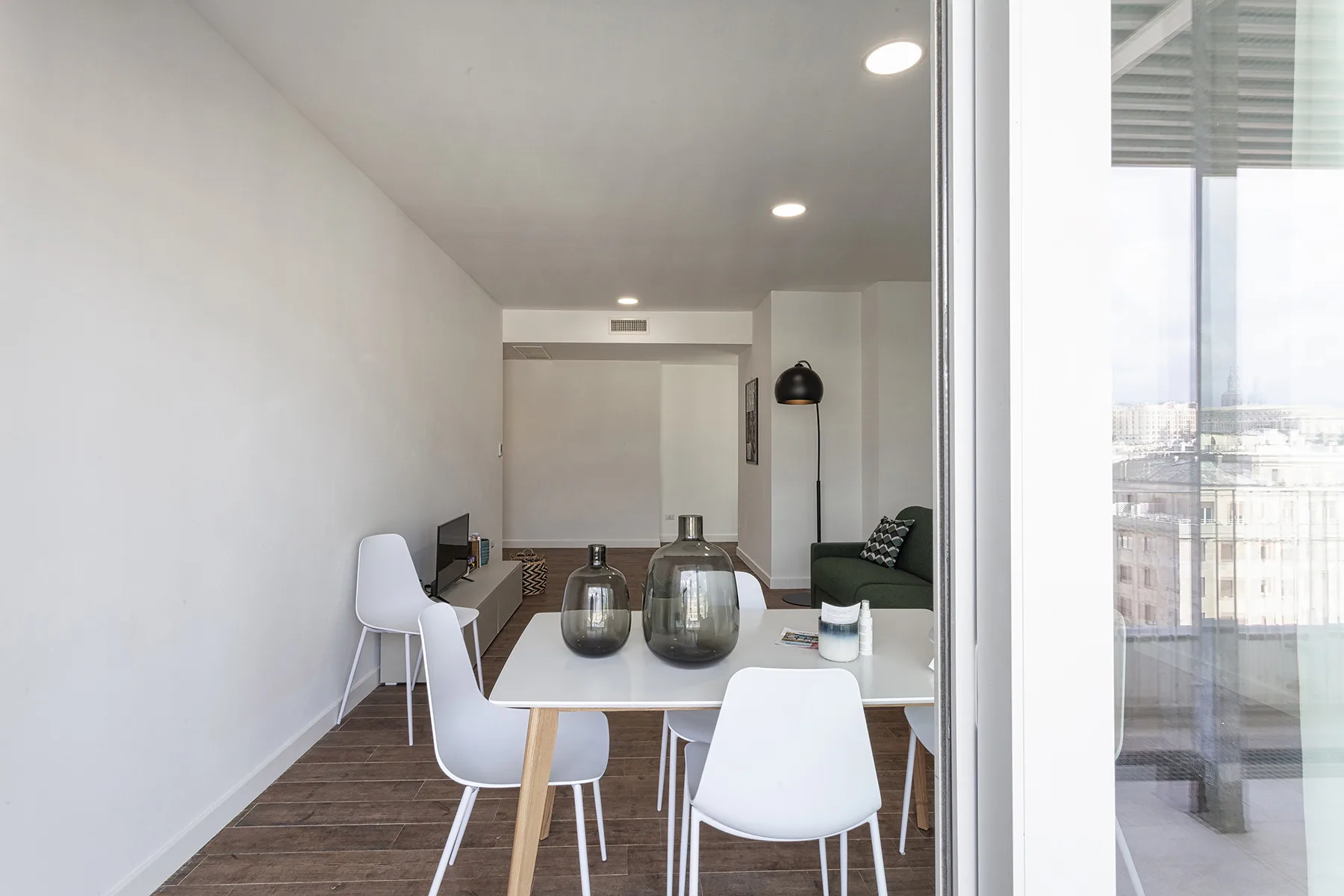 Un comedor con una mesa y sillas blancas da a un balcón.
